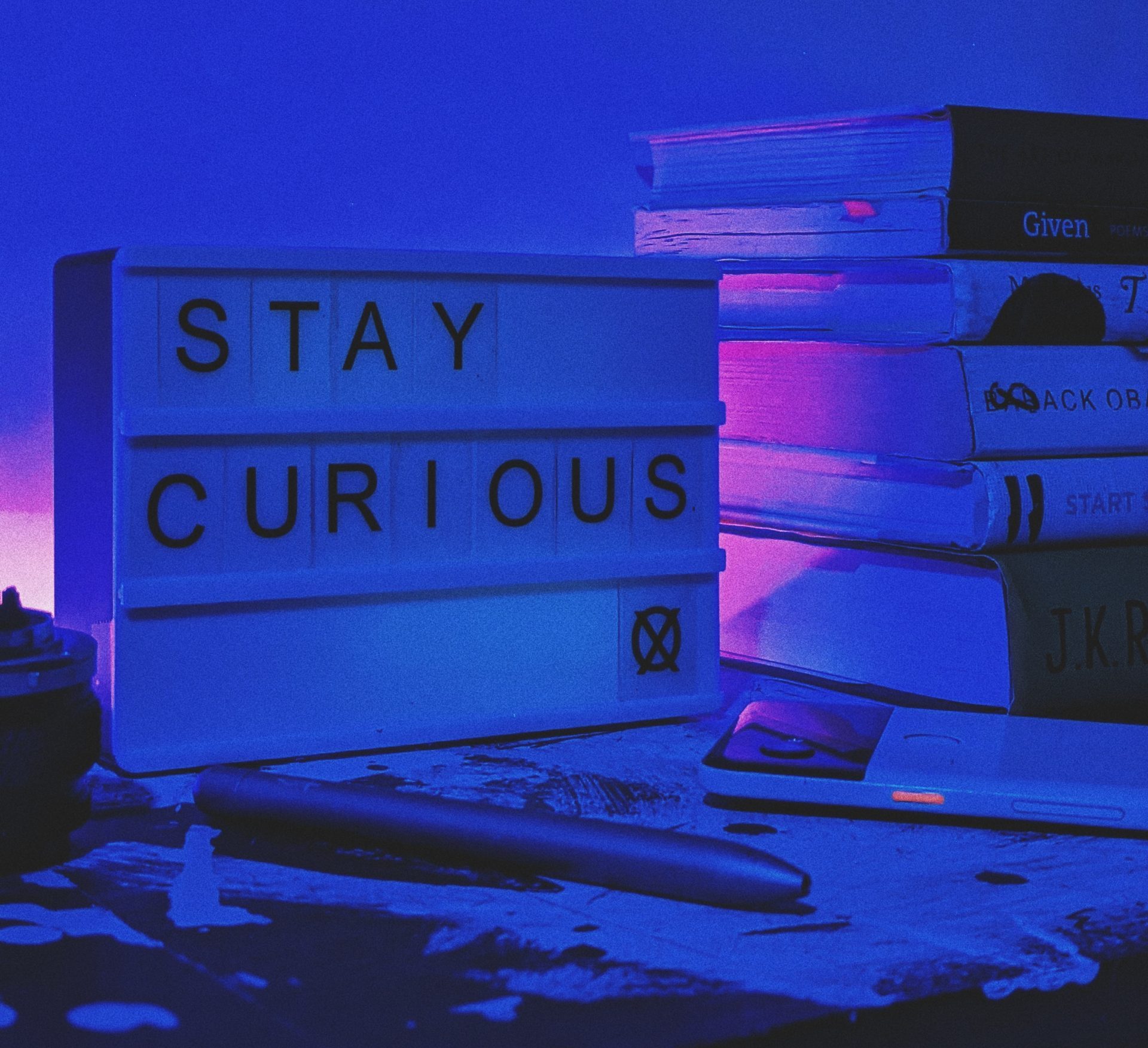 A sign reading "stay curious" in front of a stack of books